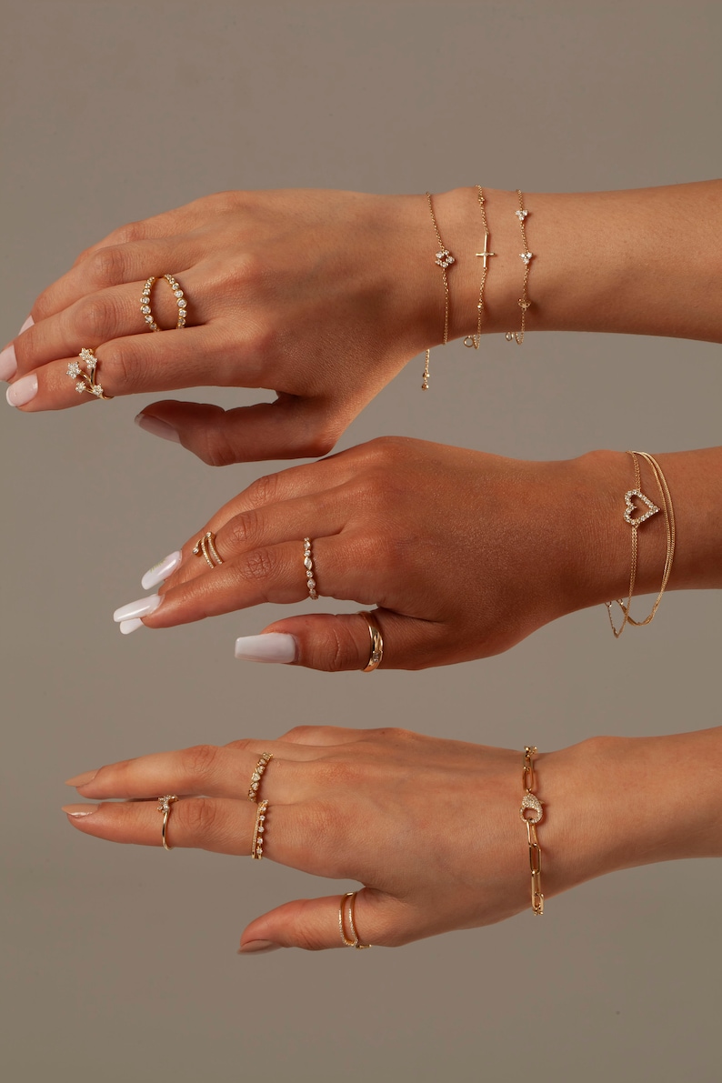 May include: A set of gold jewelry featuring delicate diamond-encrusted rings and bracelets. The jewelry includes a heart-shaped bracelet, a cross bracelet, and several rings with different designs.