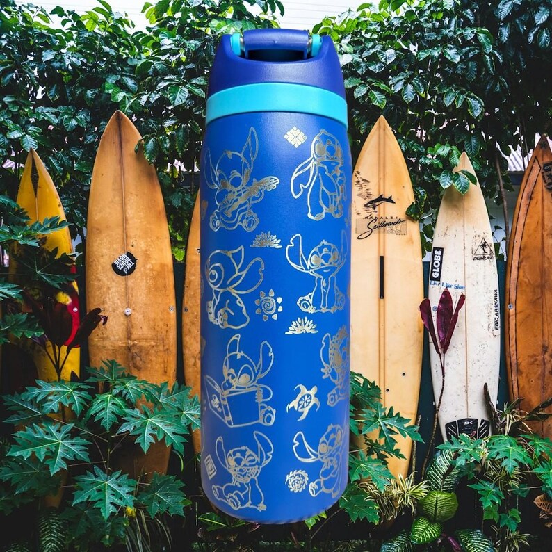 May include: Blue water bottle with gold cartoon character illustrations. It has a blue handle and a light blue band. The background features surfboards and green foliage. The bottle is approximately 25 cm tall.