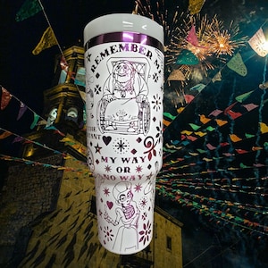 May include: White travel mug with a purple rim and lid. The mug features a black and purple illustration of a character from the movie Coco, with the words "REMEMBER ME" and "MY WAY OR NO WAY".