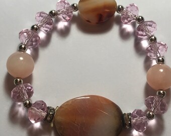May include: A beaded bracelet featuring large oval and round stones in shades of brown and pink. The bracelet is strung with smaller faceted pink beads and silver-colored metal beads.