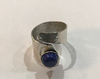 May include: A silver ring with a hammered finish and a blue gemstone set in the center.
