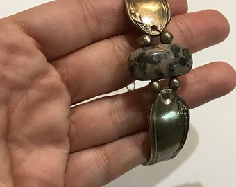 May include: A silver spoon bracelet with a brown and white stone bead. The bracelet is made from a bent spoon and has a decorative design on the spoon.