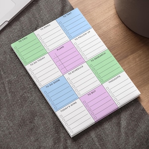 May include: A multi-coloured notepad with sections for tasks like "To Call," "To Email," and "To Text." Each section is a different pastel shade, with checkboxes. The notepad is on a wooden desk, near a laptop.