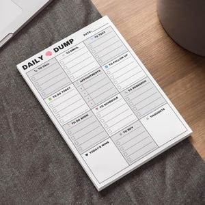 Op de afbeelding: Een witte notitieblok met de woorden "DAILY DUMP" en selectievakjes voor taken zoals "To Call", "To Email" en "To Do Today". Het notitieblok ligt op een donkergrijze ondergrond.
