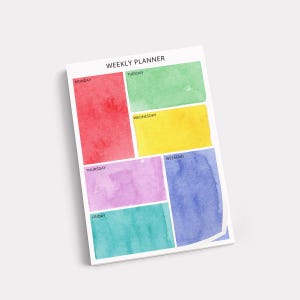 May include: Weekly planner notepad with watercolor blocks in red, green, yellow, purple, teal, and blue. The days of the week are labeled in white text. The notepad is angled on a white background.
