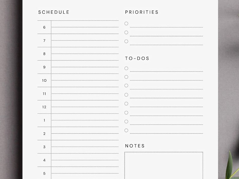 Close-up of a minimalist daily planner PDF printed on A4 paper with half-hourly schedule and to-do list columns, photographed flat on a light wooden surface with a pencil and paper clips in view.