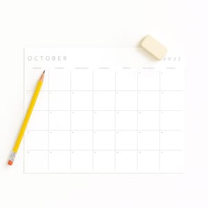 October 2027 printable monthly calendar displayed on a white surface with a yellow pencil and eraser.