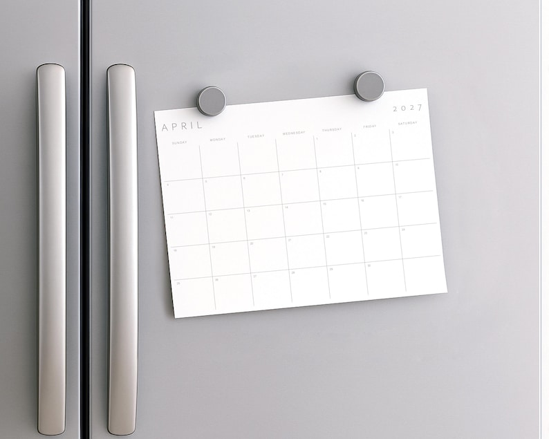 Printable 2027 monthly calendar attached to a wall with magnets beside a modern silver radiator.