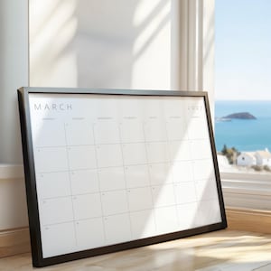 March 2027 printable monthly calendar displayed in a black frame beside a bright window with an ocean view.