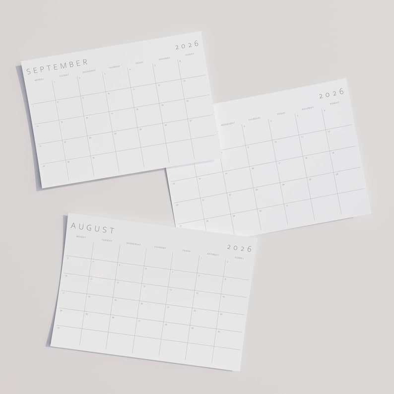 Close-up of a landscape 2026 monthly planner on A4 paper, clean grey lines and modern sans-serif typography, held above a neutral flat surface.