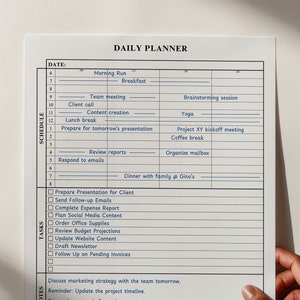 A "daily planner" template on a white sheet of paper held by a hand against a light beige background.