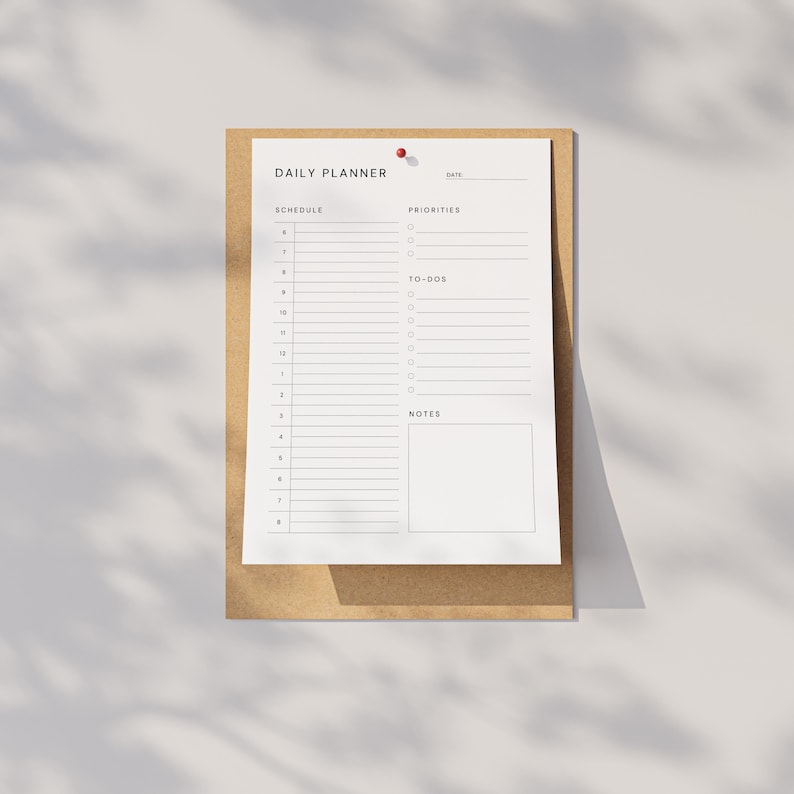A printed PDF daily planner sheet on a flat white surface, showing date line, priorities, to-do list, and notes sections, next to a gold pen and paper clips arranged neatly.