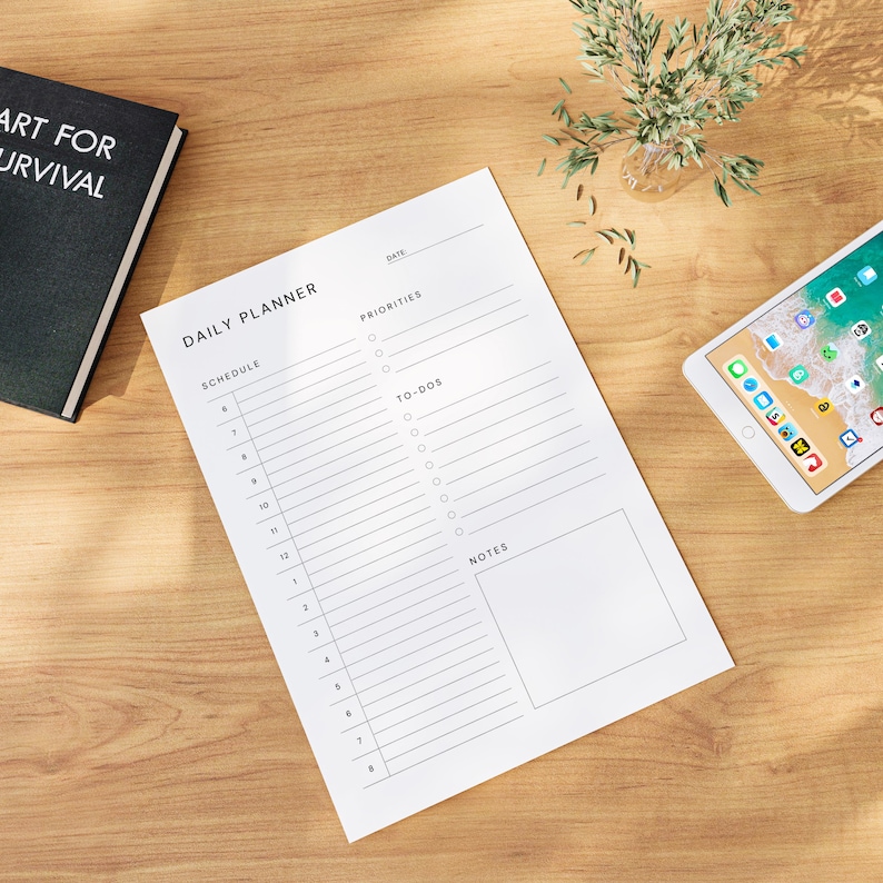 A printed daily planner layout with clean black lines and modern typography, photographed on neutral fabric background with subtle shadows and soft natural light.