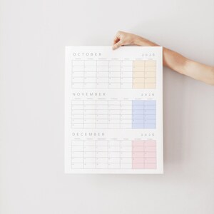 May include: A white 2026 calendar featuring the months of October, November, and December. Each month has a grid layout with days of the week. The calendar has color-coded sections in yellow, blue, and pink.
