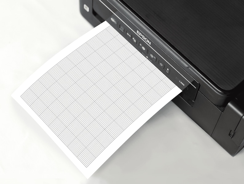 A white A4 sheet of printable 10x10 graph paper with fine grey grid lines, placed on a neutral desk background, showing the uniform ten-per-inch square pattern for drawing, writing, or technical sketches.