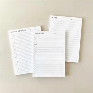 May include: Three white notepads with black text. One notepad reads "TODAY'S SCHEDULE" with a time scale. Another reads "TO DO LIST" with checkboxes. The third notepad reads "NOTES". All have lined pages.