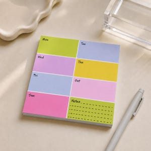 May include: A rectangular weekly planner notepad featuring eight colorful sections for each day of the week from Monday to Sunday, plus a notes section. The blocks are colored in lime green, light blue, purple, yellow, and pink with black text labels.