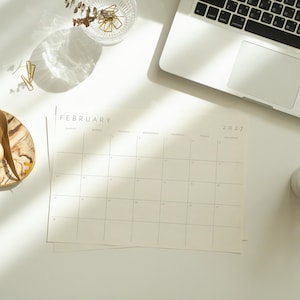 Printable 2027 monthly planner displayed on a bright desk beside a laptop, coffee cup, and modern accessories.