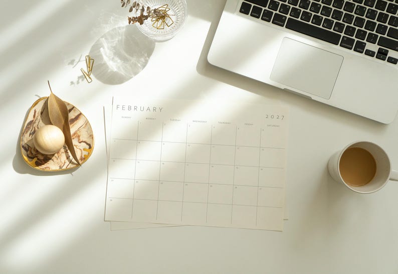 Printable 2027 monthly planner displayed on a bright desk beside a laptop, coffee cup, and modern accessories.