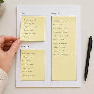 May include: A white planner sheet with black text headers for Daily, Weekly, and Monthly tasks. The sheet features yellow sticky notes with handwritten lists including items like Morning stretch, Grocery shop, and Budget review. A black pen lies nearby.