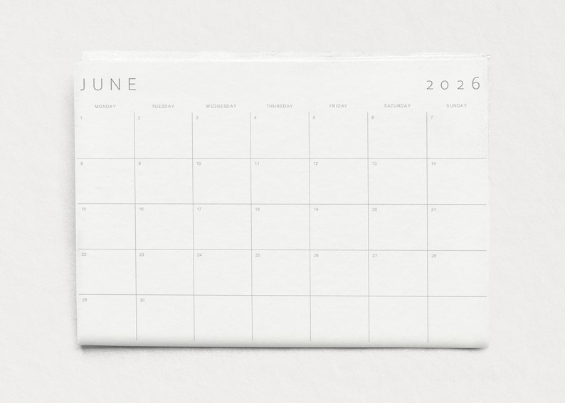 Close-up of a single 2026 monthly planner page in landscape format, grey modern typography and subtle lines on white paper held by a hand against a neutral wall.
