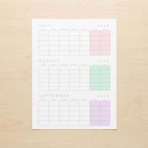 May include: A white paper calendar for July, August, and September 2026. Each month's grid is in a light gray font. July has a pink highlight, August has a green highlight, and September has a purple highlight. The calendar is on a light wood surface.