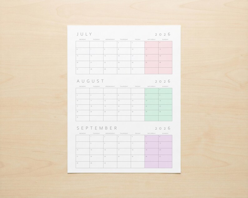 May include: A white paper calendar for July, August, and September 2026. Each month's grid is in a light gray font. July has a pink highlight, August has a green highlight, and September has a purple highlight. The calendar is on a light wood surface.