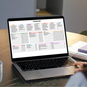 A laptop computer with a black keyboard and a black trackpad. The screen displays a digital to-do list with a colourful grid and the text "TO-DO LIST".