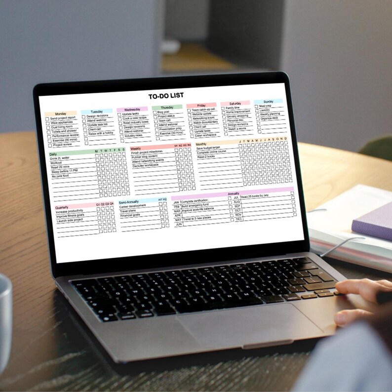 A laptop computer with a black keyboard and a black trackpad. The screen displays a digital to-do list with a colourful grid and the text "TO-DO LIST".