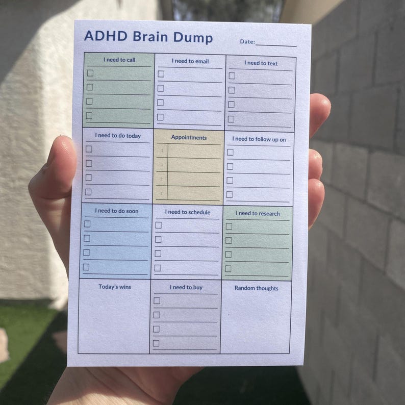 A hand holds a 4x6 ADHD planner pad in natural light, showing sections for To Do, Calls, Email, and Notes, with a backyard background of blurred green foliage and soft shadows.