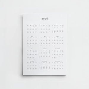 Digital download 2026 calendar printed on Tabloid paper, held up by a person in a white shirt, displaying minimalist typography with a full year view in portrait orientation.