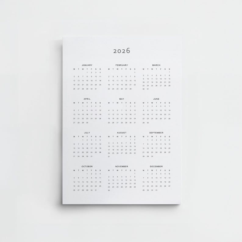 Digital download 2026 calendar printed on Tabloid paper, held up by a person in a white shirt, displaying minimalist typography with a full year view in portrait orientation.