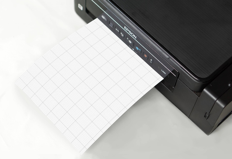 Stack of printable graph-paper sheets with 10 squares-per-inch grid, viewed from above, edges aligned neatly, showing repeated small square pattern across all pages.