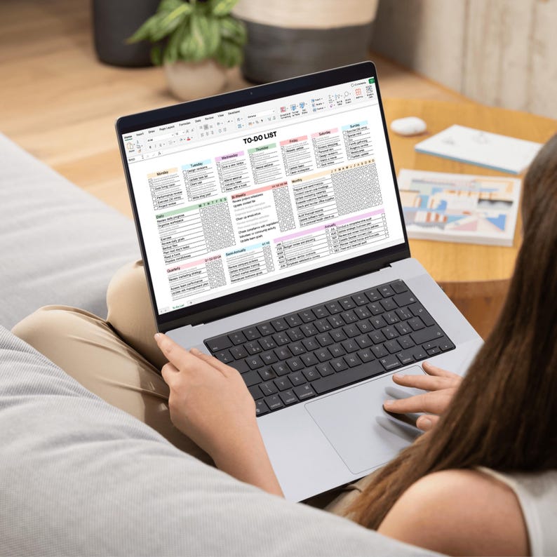 A person working on a laptop computer with a to-do list spreadsheet open on the screen. The spreadsheet is divided into columns for each day of the week and includes tasks to be completed.