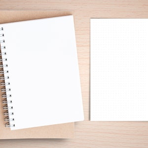 May include: A brown notebook with a white spiral bound notebook on top of it. A white sheet of paper with small dots is on the right side of the image.