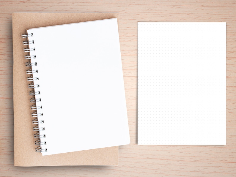 May include: A brown notebook with a white spiral bound notebook on top of it. A white sheet of paper with small dots is on the right side of the image.