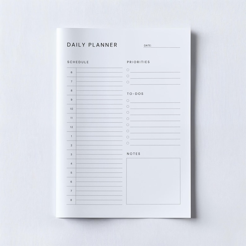 Printable daily planner sheet in A4 format with a simple layout and clear typography, displayed beside minimal stationery and a cup of tea on a light-toned workspace.