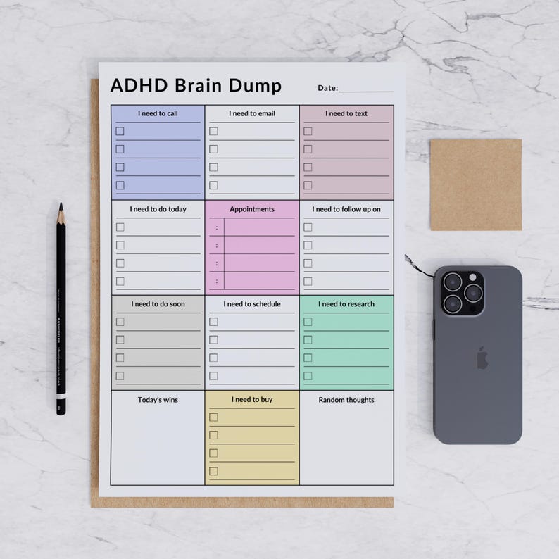 A printed ADHD brain dump planner showing detailed sections for tasks, phone calls, and reminders. The planner is on a light, neutral surface, clearly showing its portrait orientation and readable fonts.