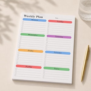 May include: A white weekly plan notepad with colorful headers for each day of the week. The notepad includes a gold pen and a glass of water. The notepad has the text "Weekly Plan" at the top.