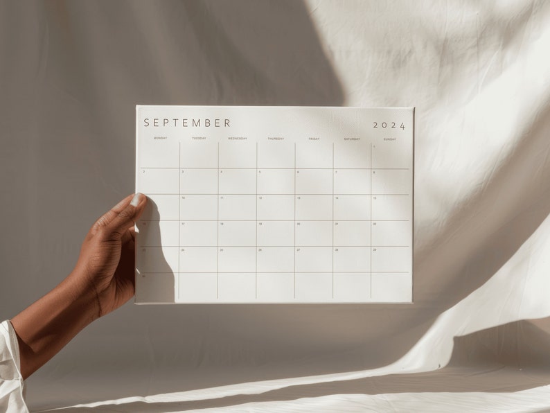 Elegant monthly planner held by a person's arm against a serene beige backdrop, offering organized scheduling for the month ahead.