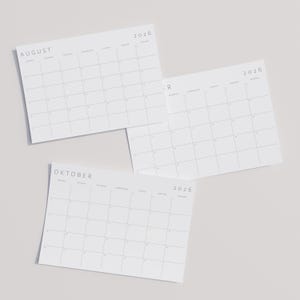 2026 Monatskalender auf A3-Papier im Querformat mit minimalistischen grauen Linien und moderner Typografie, liegend auf neutraler Oberfläche.