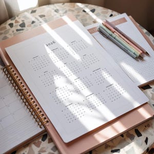 2026 calendar printable sheet displayed on white paper with full year overview grid and minimalist grey typography, placed on a neutral desk surface with simple and clean styling