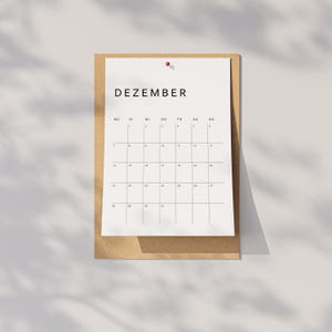 Monatsübersicht aus dem Kalender 2026 Deutsch, gedruckt im minimalistischen Stil auf weißem Papier, klare Linien und moderne Typo, liegt auf neutraler beige-grauer Oberfläche.