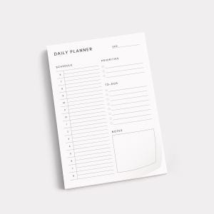 May include: A white daily planner notepad with the words "DAILY PLANNER" at the top. The notepad includes sections for schedule, priorities, to-dos, and notes. The notepad is angled slightly, showing a corner of the pad.