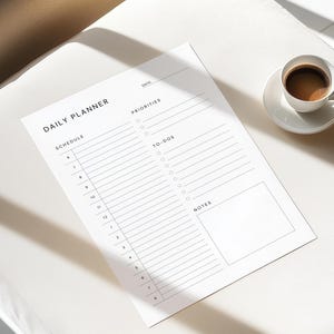 The daily planner template printed on crisp white paper with sections labeled schedule, priorities, and notes, displayed beside a laptop and coffee cup on a tidy white desk.