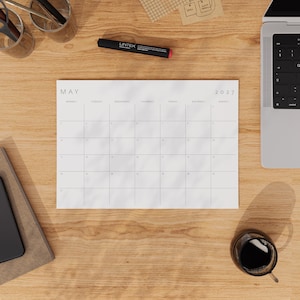 May 2027 printable monthly calendar placed on a wooden desk beside a keyboard, stationery, and coffee.