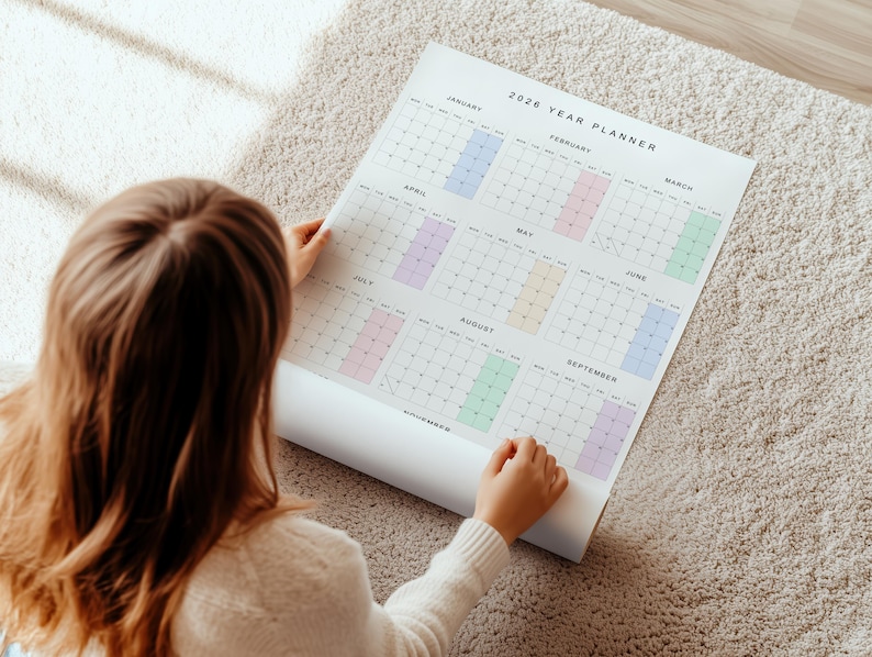 Overhead flat lay of 2026 wall calendar on white paper, portrait layout, vibrant pastel month headers, full-year grid visible, clean design showing weekdays and all dates clearly.