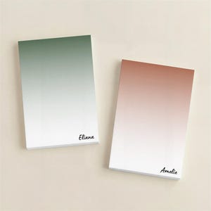 May include: Two rectangular notepads with a gradient design. One transitions from green to white, the other from a reddish-brown to white. The name "Eliana" is printed on the green notepad, and "Amelie" on the other.