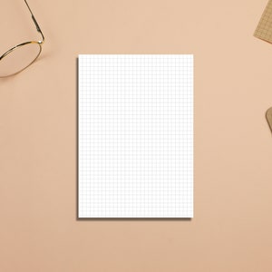 May include: A white gridded notepad on a light brown surface with a pair of gold-rimmed glasses and a brown clipboard with lined paper.