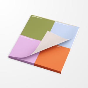May include: A colorful notepad with a quadrant design, featuring sections in olive green, light blue, lavender, and orange. The top sheet is partially lifted, revealing the blank underside. Each section has text that reads "urgent & important" and "not urgent".